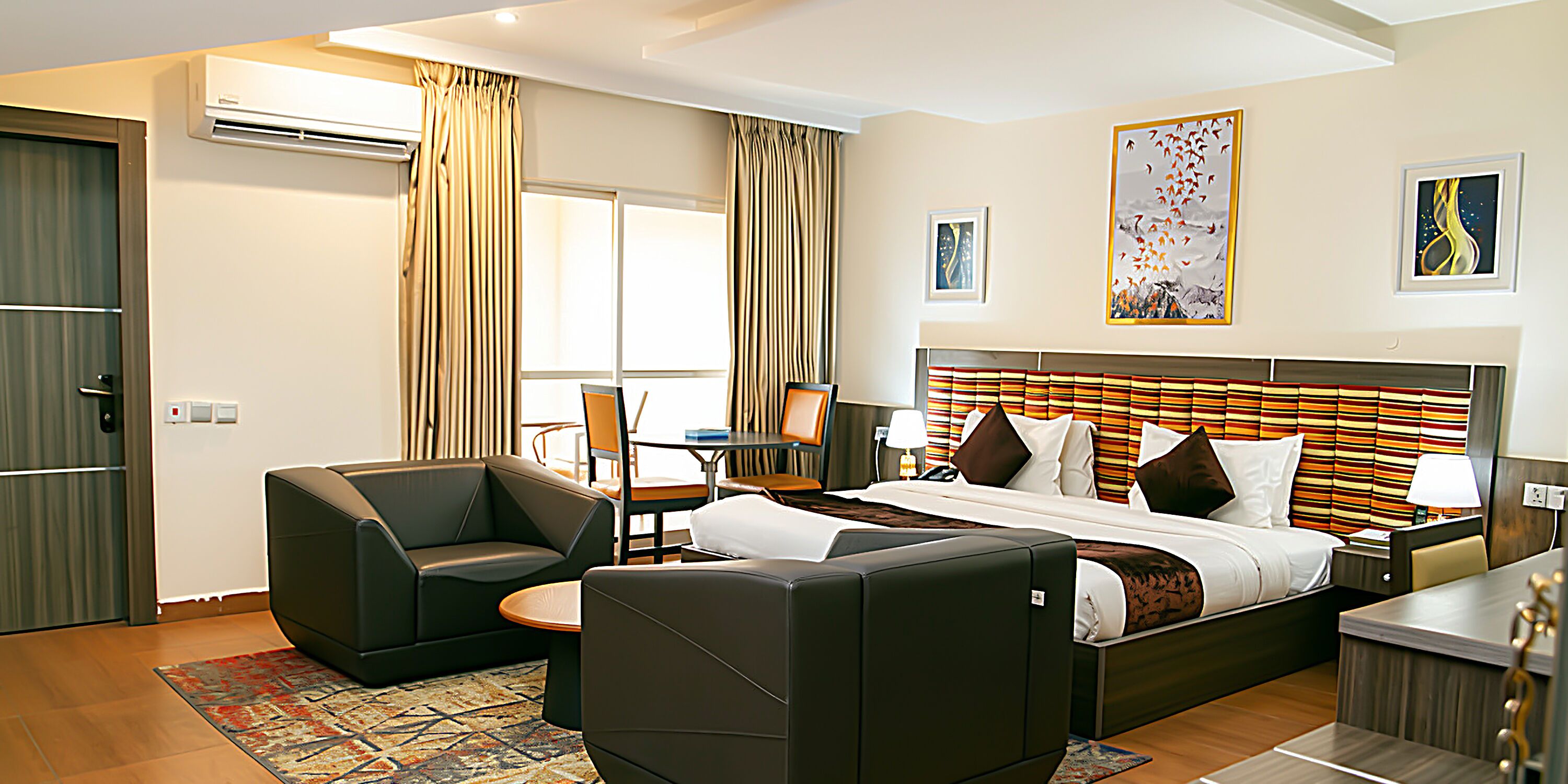A hotel room with a bed, two armchairs, a desk, and a dining table.