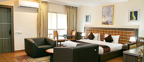 A hotel room with a bed, two armchairs, a desk, and a dining table.