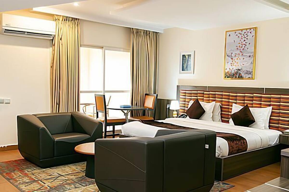 Een hotelkamer met een bed, twee fauteuils, een bijzettafeltje, een bureau en een raam met gordijnen.