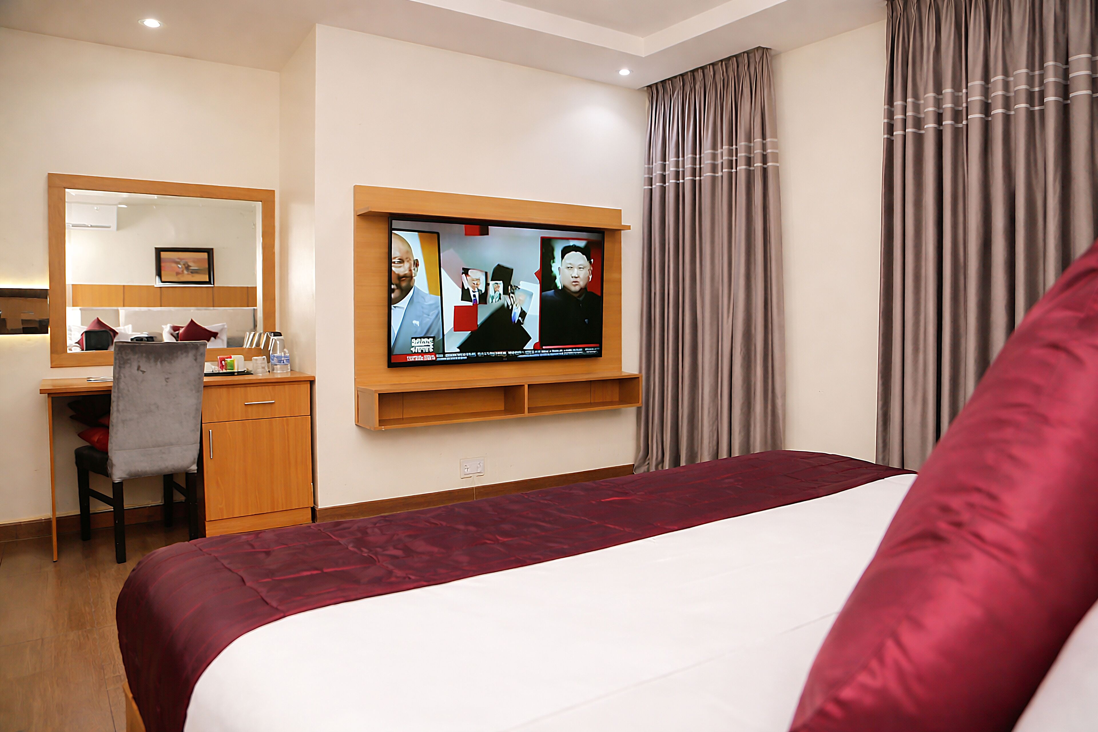 A hotel room with a bed, a desk, a chair, a television mounted on the wall, and a window with curtains.