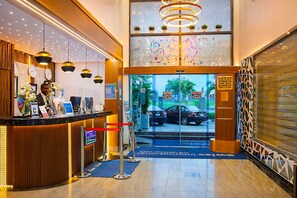 Een hotel receptie met een receptiebalie, een klok en een glazen deur naar buiten.