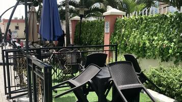 An outdoor seating area with tables and chairs, surrounded by a metal fence and greenery.