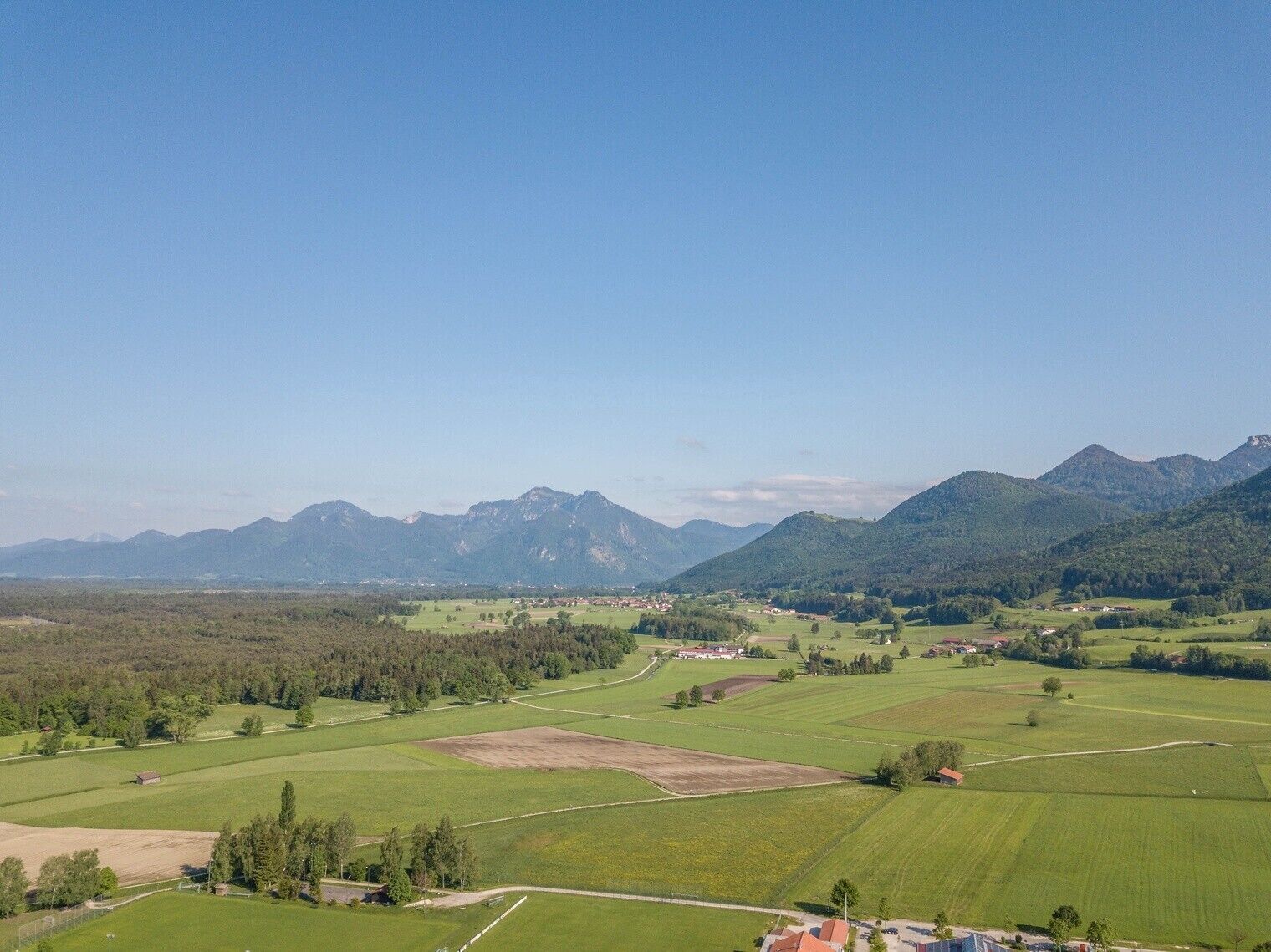 Un paysage rural avec des champs, des maisons éparpillées et des montagnes en arrière-plan.