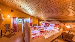 Un dormitorio acogedor con techo de madera, una cama con ropa de cama a cuadros, una mesita de noche y una silla.