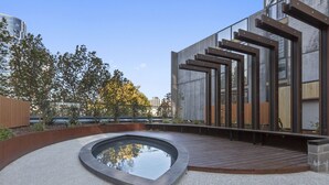 A modern outdoor area with a circular water feature, wooden deck, and a building with a unique architectural design.