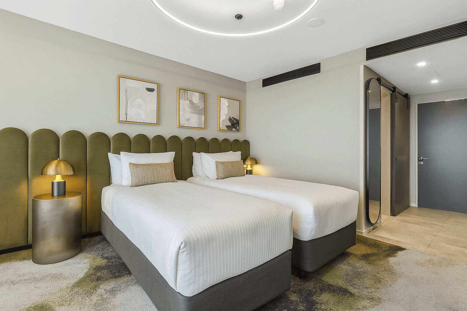 Ett modernt hotellrum med två sängar, en rund taklampa och konstverk på väggen.