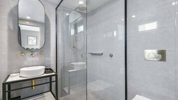 A modern bathroom with a glass-enclosed shower, a white sink, and a large mirror.