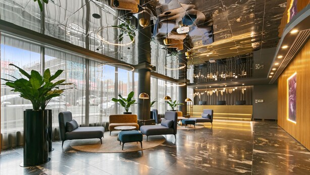 A spacious lobby with modern furniture, large windows, and a high ceiling with unique lighting fixtures.
