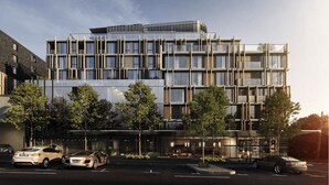 A modern multi-story hotel with a glass facade, outdoor seating area, and a parking lot.
