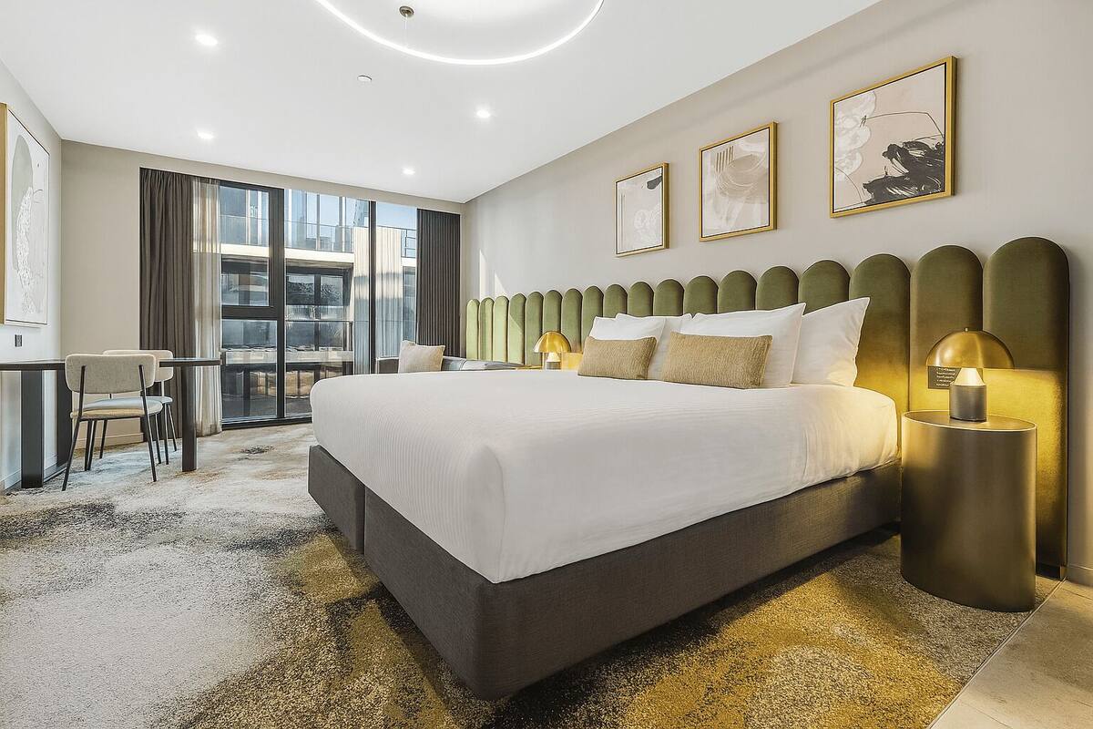Habitación de hotel moderna con una cama grande, un escritorio y vistas de la ciudad a través de amplios ventanales.