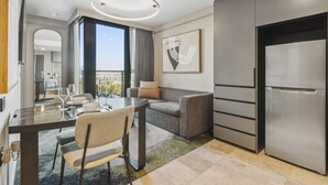 A modern kitchen with a dining area, a sofa, and a large window offering a city view.