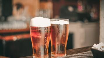 Two glasses of beer on a wooden table with a bowl of snacks and a napkin.