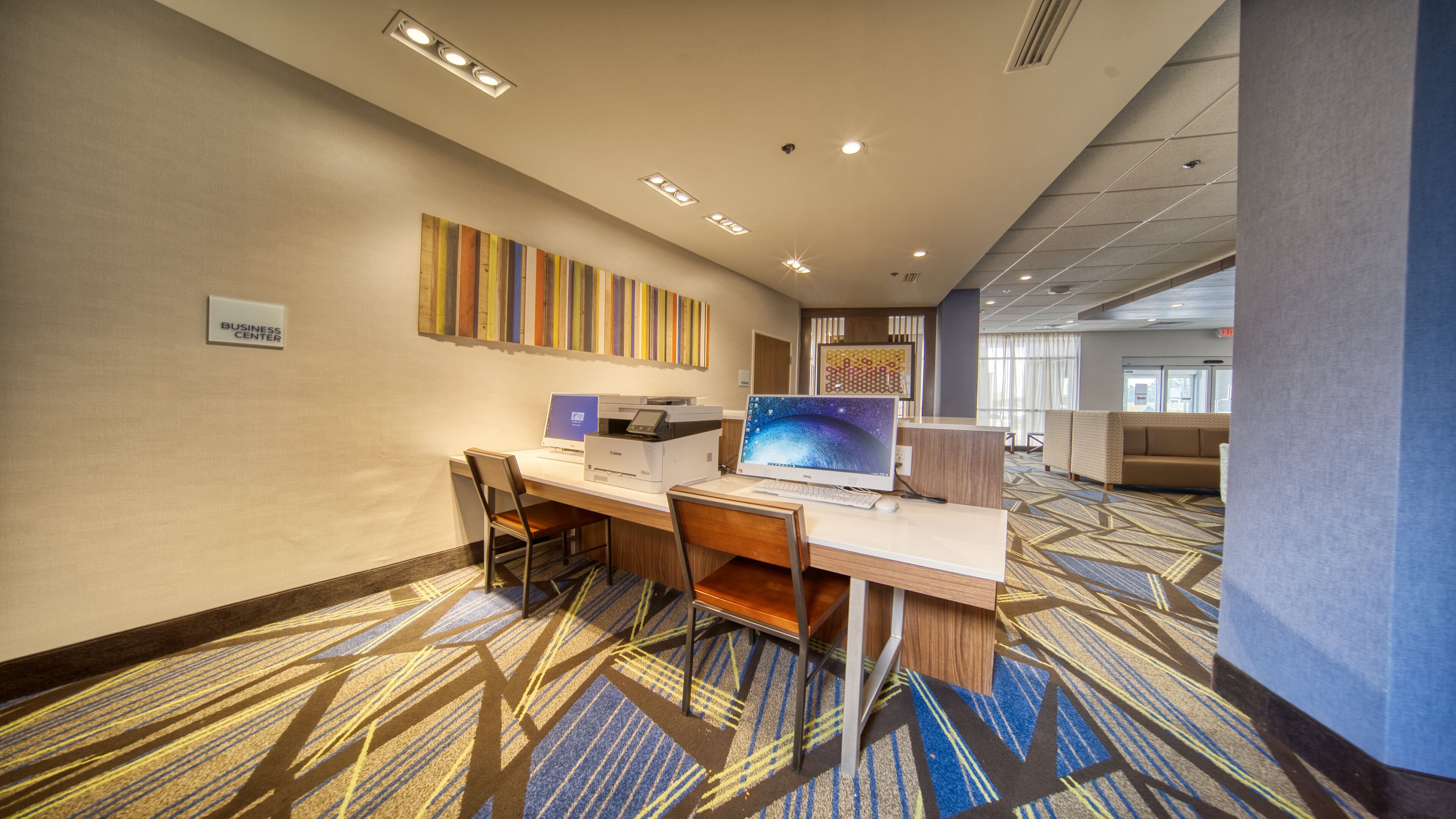 A hotel business center with a reception desk, computers, and a large window.