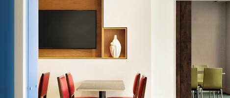 Habitación de hotel con comedor que incluye una mesa y sillas, una obra de arte grande enmarcada en la pared y vista de la habitación contigua.
