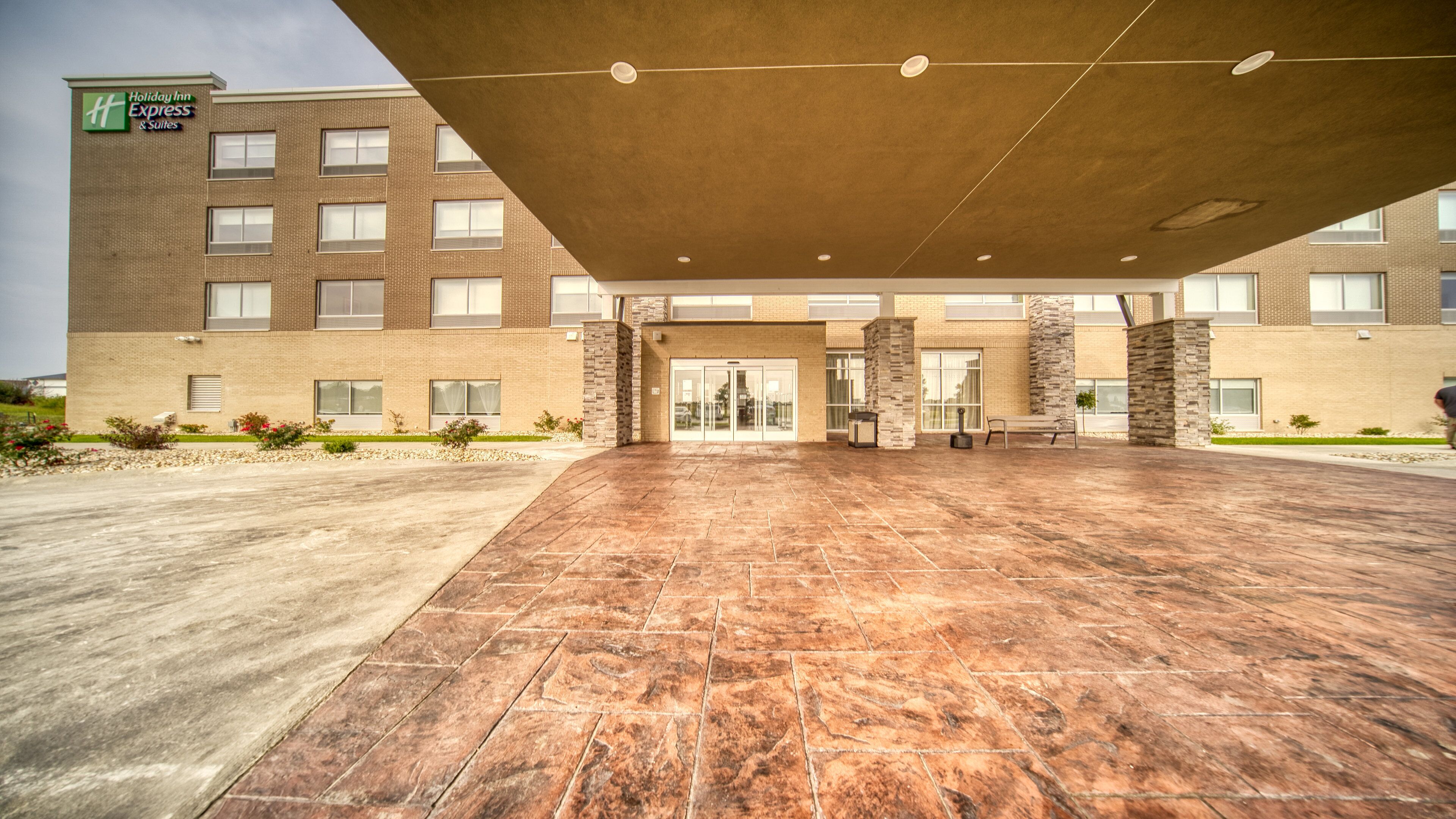 A Holiday Inn Express & Suites with a spacious entrance, a covered waiting area, and a brick facade.