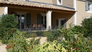 Un bâtiment à deux étages doté d’un patio couvert, d’une petite fenêtre et d’un jardin où poussent différentes espèces de plantes.