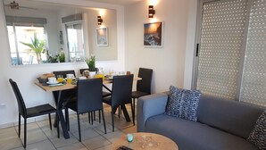 A modern living room with a gray sofa, a coffee table, and a dining area with chairs and a table set for breakfast.