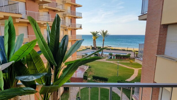 A balcony with a view of a beach, palm trees, and a well-maintained lawn.