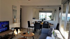 A living room with a TV, a sofa, a coffee table, and a dining area with chairs and a table.