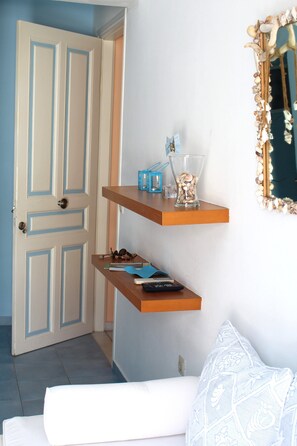A room with a door, a white couch, and a wall-mounted shelf with decorative items. - Innaxos City Central Studio (Naxos)
