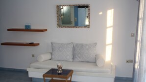 A living room with a white sofa, two cushions, a small table, and two floating shelves. - Innaxos City Central Studio (Naxos)