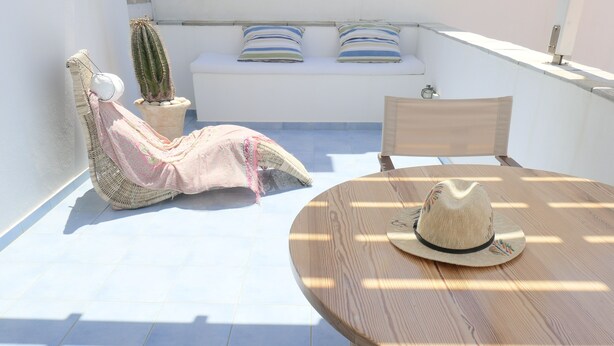 A sunlit patio with a round wooden table, a woven chair, a sofa with striped cushions, and a cactus plant. - Innaxos City Central Studio (Naxos)