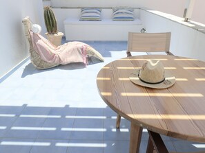 A sunlit patio with a round wooden table, a woven chair, a sofa with striped cushions, and a cactus plant. - Innaxos City Central Studio (Naxos)