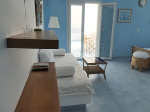 A modern living room with a sofa, a small table, and a bench. There is a balcony with a view of the sea.