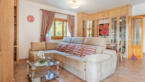 A living room with a sofa, a glass coffee table, a clock, and wooden cabinets. - Cosy Holiday Home "Solluna" with Wi-Fi, Pool, Terrace and Garden with Mountain View (Son Servera)