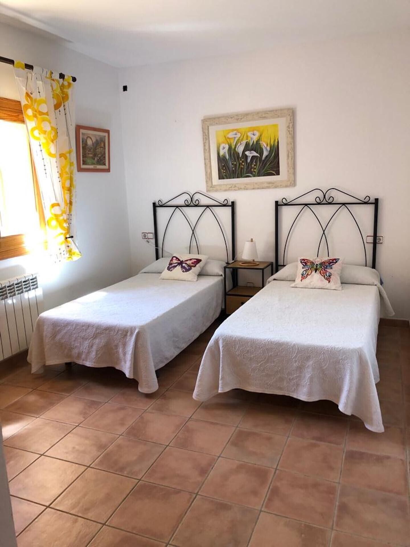 Ein Zimmer mit zwei Einzelbetten, einem Vorhangfenster, einem Heizkörper und einem Bild an der Wand.