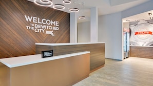 A modern hotel reception area with a wooden wall and a sign that reads "WELCOME TO BEWITCHED THE CITY".