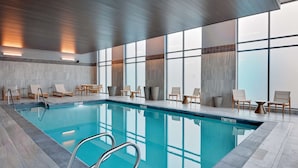 An indoor swimming pool with clear water, surrounded by lounge chairs and a tiled floor.