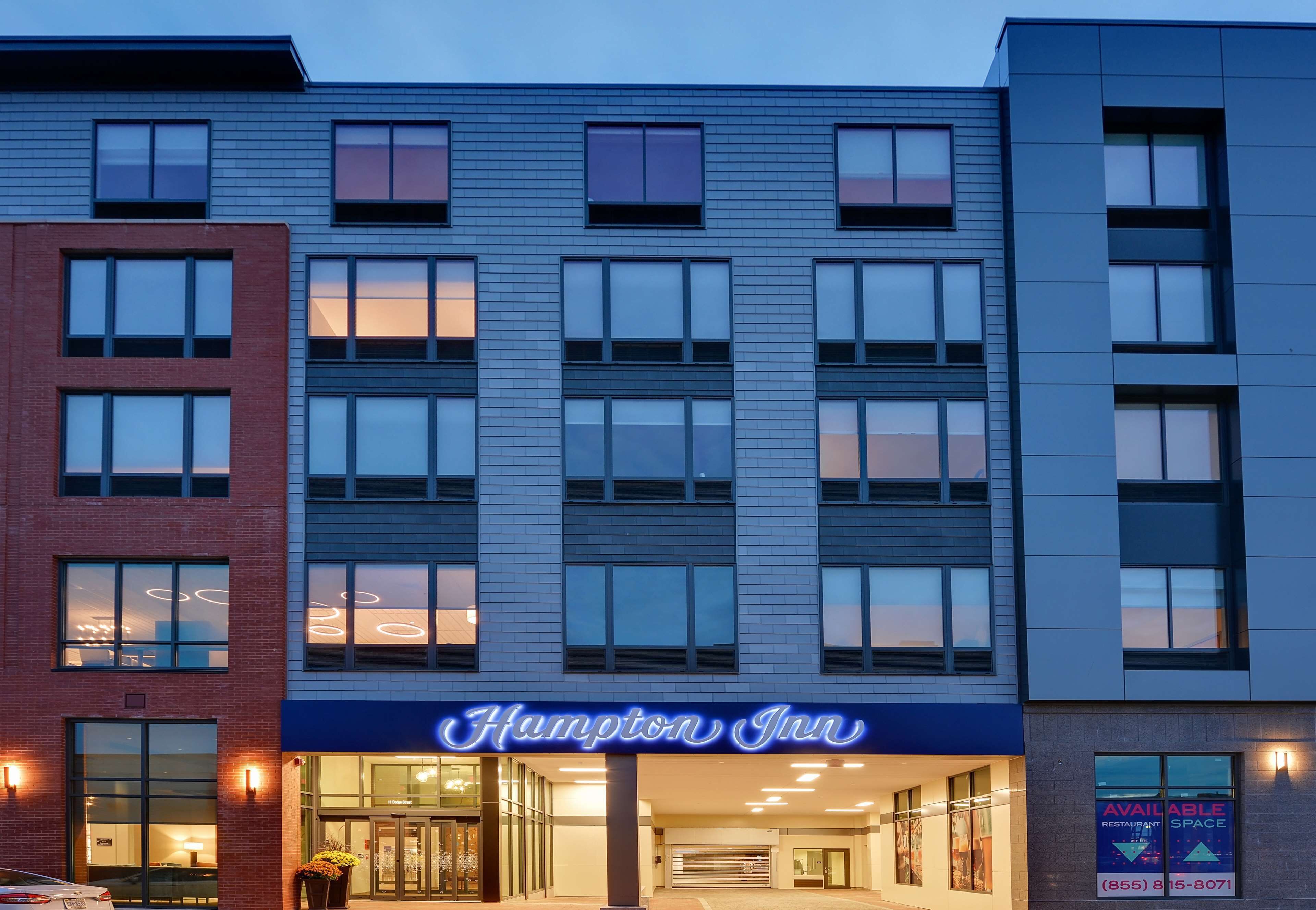 Un hotel Hampton Inn con una fachada moderna, ventanas grandes y una entrada bien iluminada.