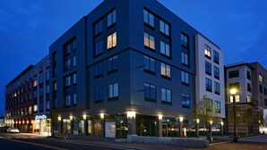 A multi-story hotel with a modern architectural design, featuring a mix of glass and dark facade, and a ground-level restaurant with illuminated signage.