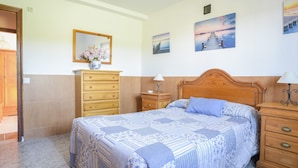 A bedroom with a bed, wooden dresser, nightstand, and wall-mounted mirror.
