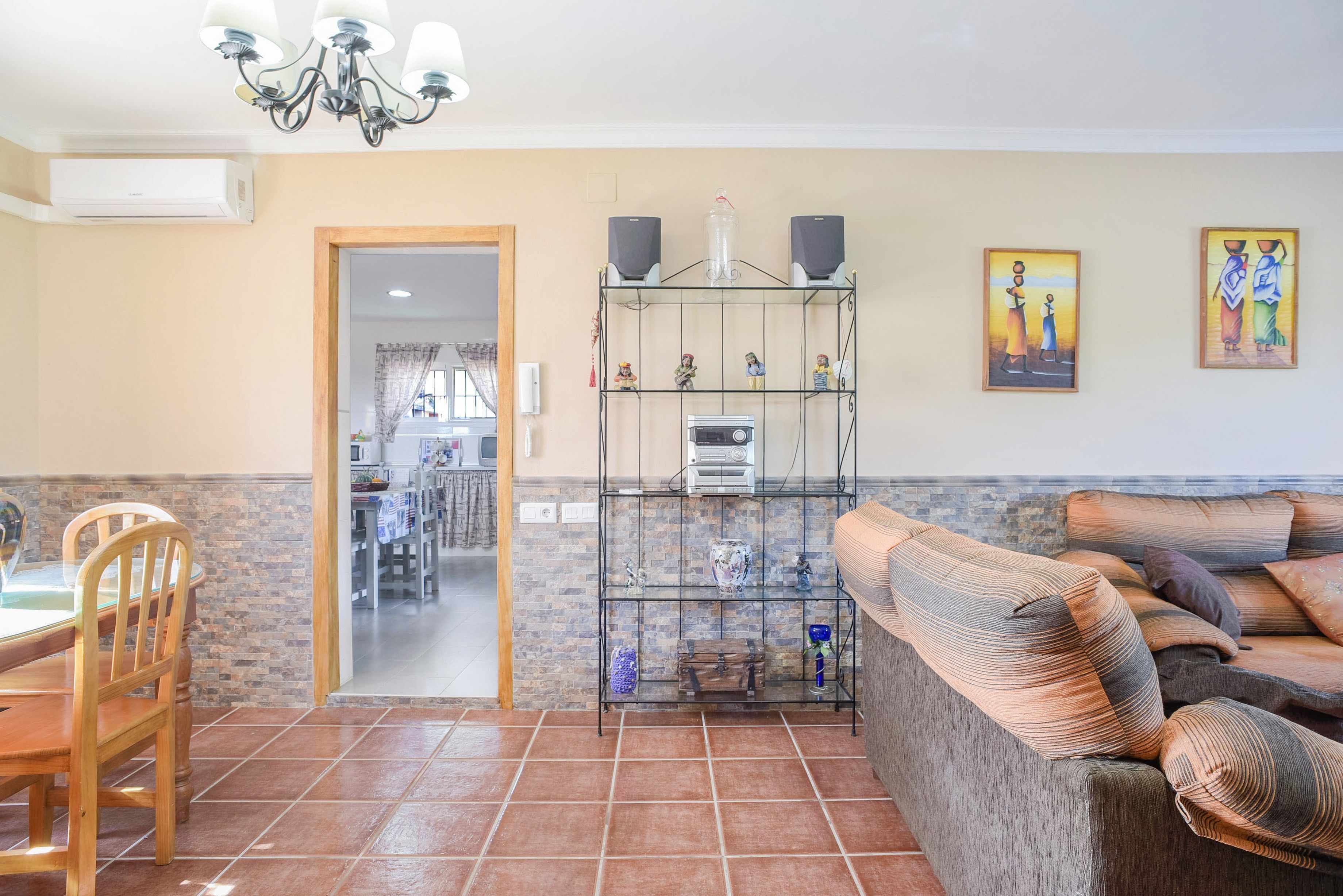 Ein Wohnzimmer mit Sofa, einem Esstisch mit Stühlen, einer Küchenzeile und einem Flur, der in ein weiteres Zimmer führt.