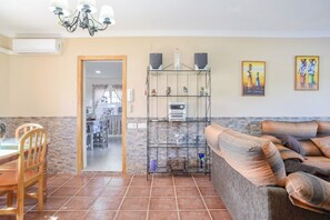 A living room with a sofa, a dining table with chairs, a kitchen area, and a hallway leading to another room.