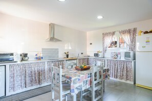 A kitchen with white cabinets, a stainless steel range hood, a microwave, a refrigerator, and a dining table with chairs.