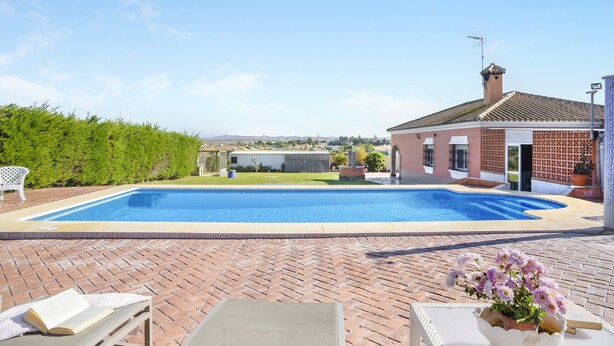A swimming pool with a brick patio, a white chair, and a flower pot.