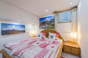 Une chambre à coucher avec un grand lit, deux tables de chevet, une fenêtre avec des rideaux et deux tableaux accrochés au mur.