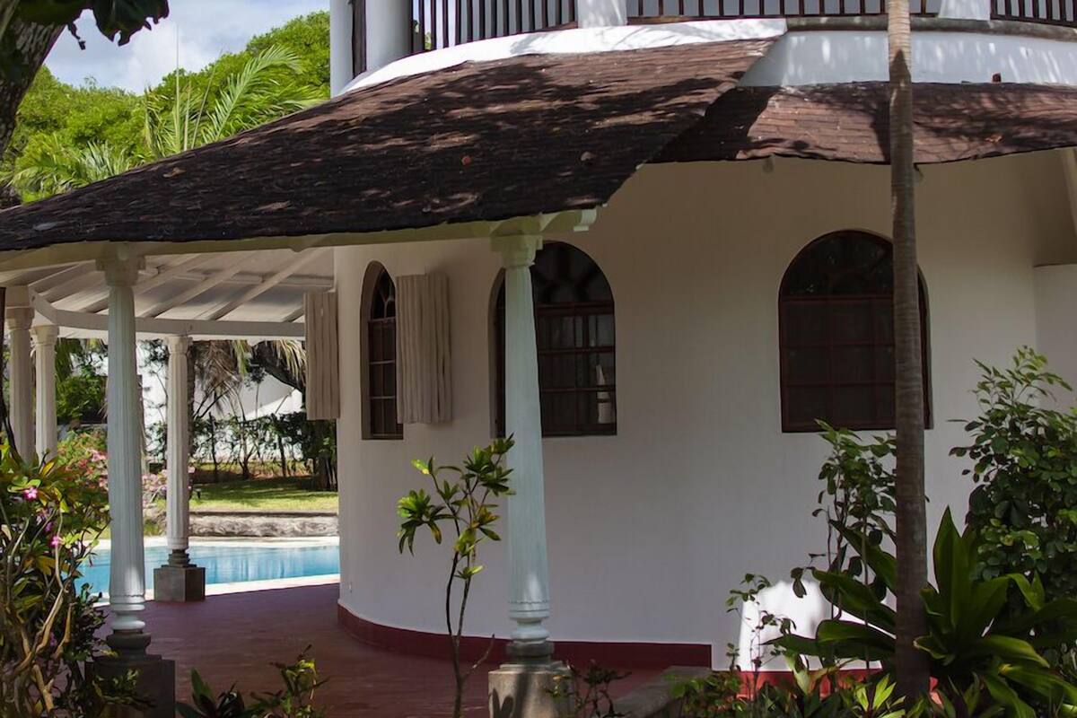 A two-story building with a covered patio, a swimming pool, and lush greenery.