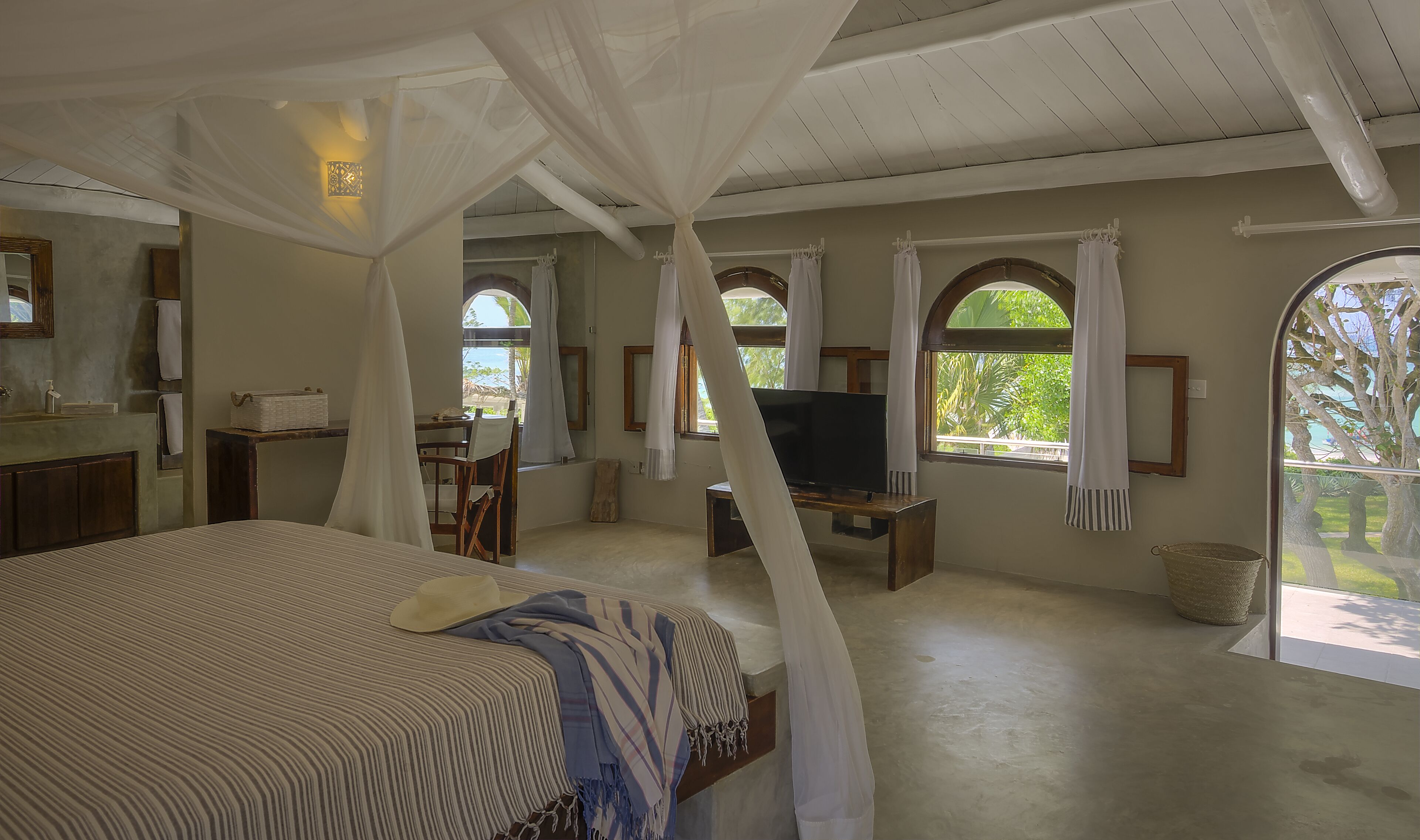 Ein Schlafzimmer mit Baldachinbett, Fernseher und einem Balkon mit Blick auf Bäume.