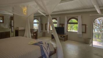 Ein Schlafzimmer mit Baldachinbett, Fernseher und einem Balkon mit Blick auf Bäume.