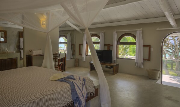 A bedroom with a canopy bed, a television, and a balcony with a view of trees. - Kobe Suite Resort (Watamu)