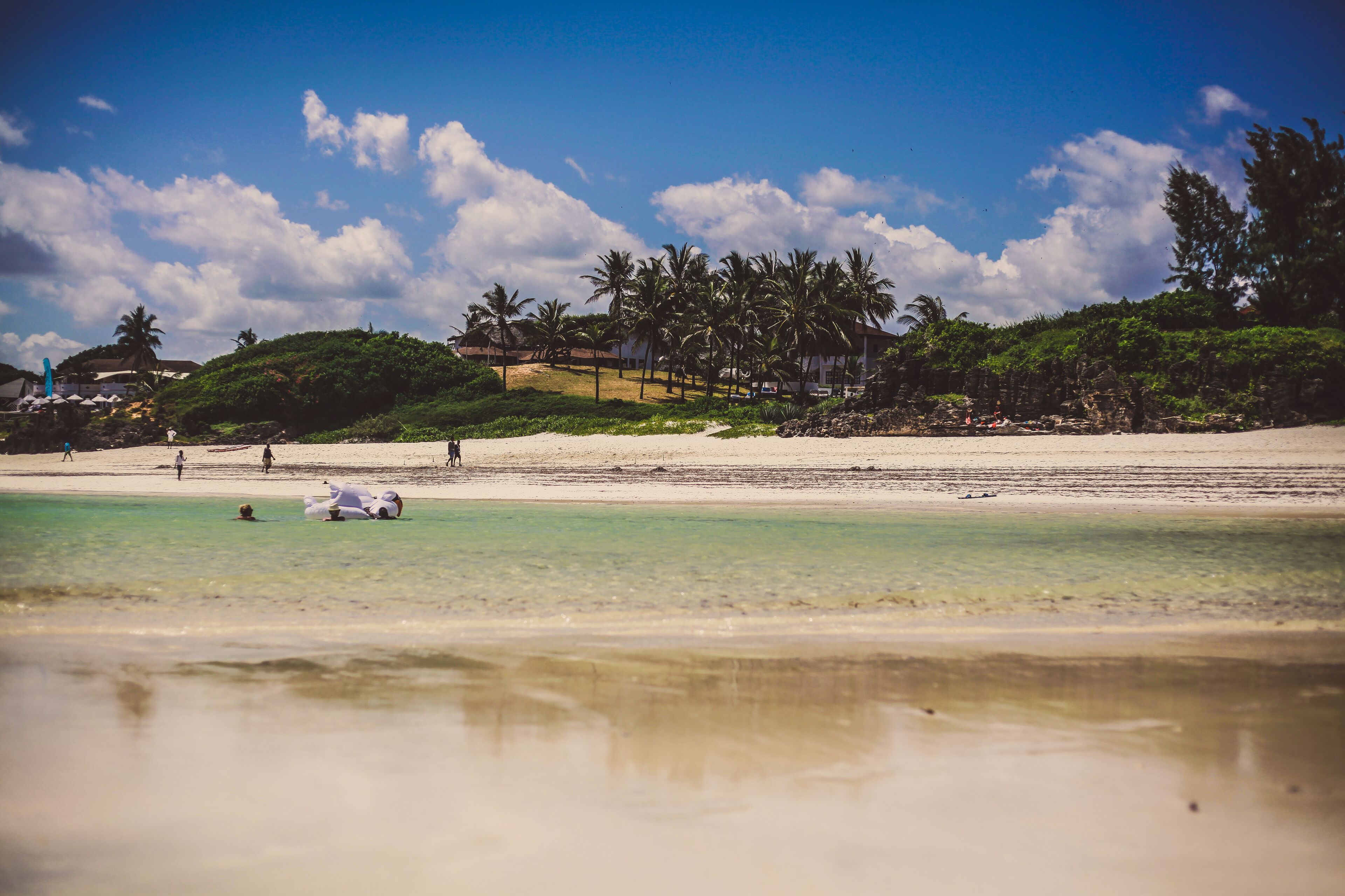 A beach with clear turquoise water, a sandy shore, and palm trees.