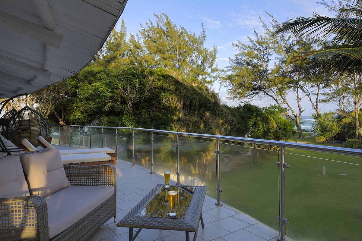 A balcony with a glass railing, a wicker sofa, and a table with two glasses of beer.