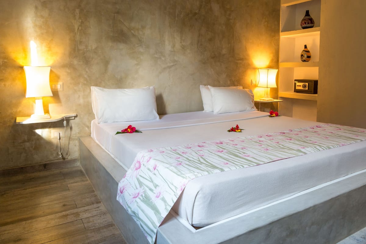 A neatly made bed with white linens and a floral-patterned bedspread, two bedside lamps, and a shelf with decorative items.