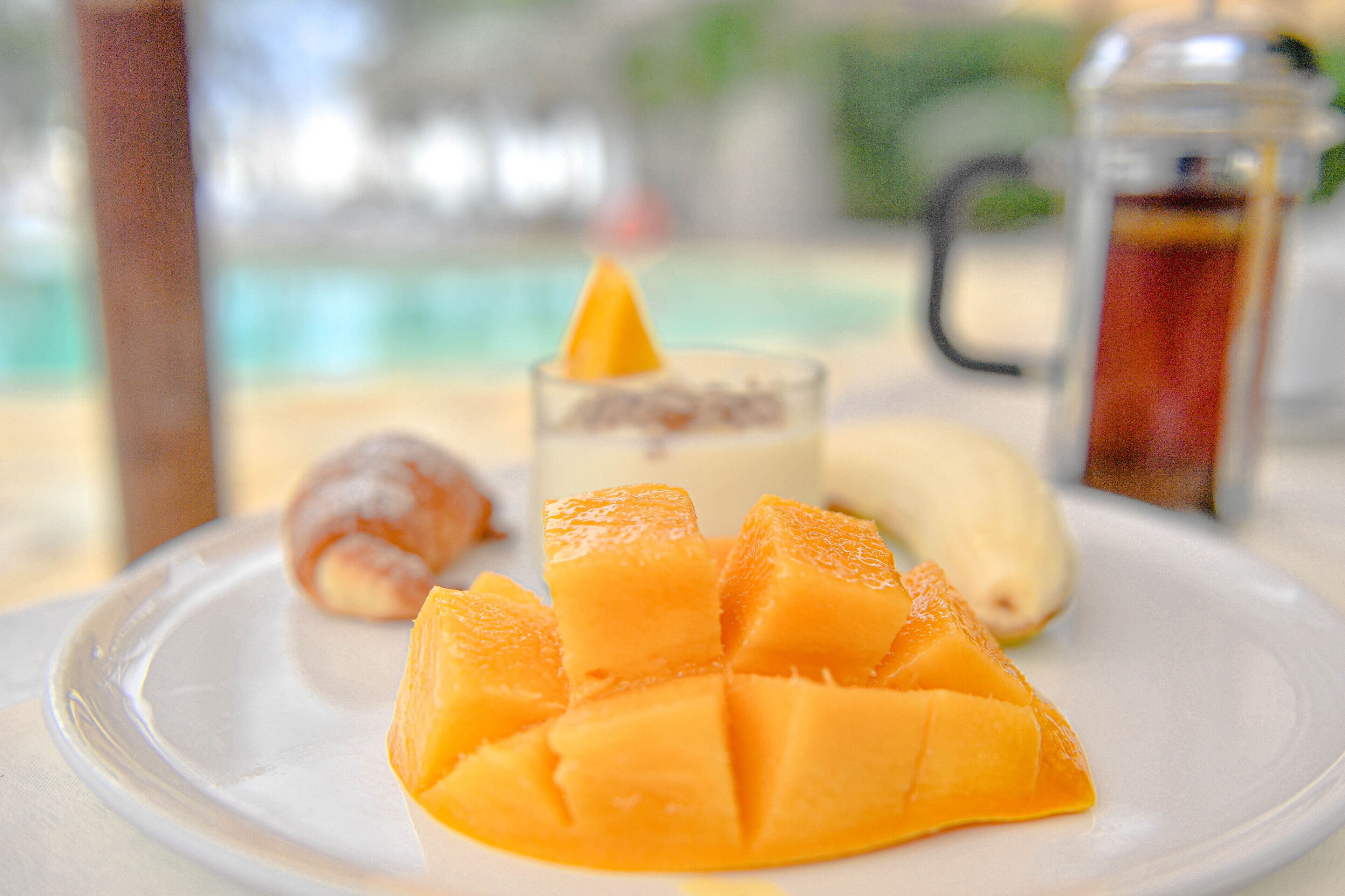 A plate with mango chunks, a glass with a yellow cone, and a banana.