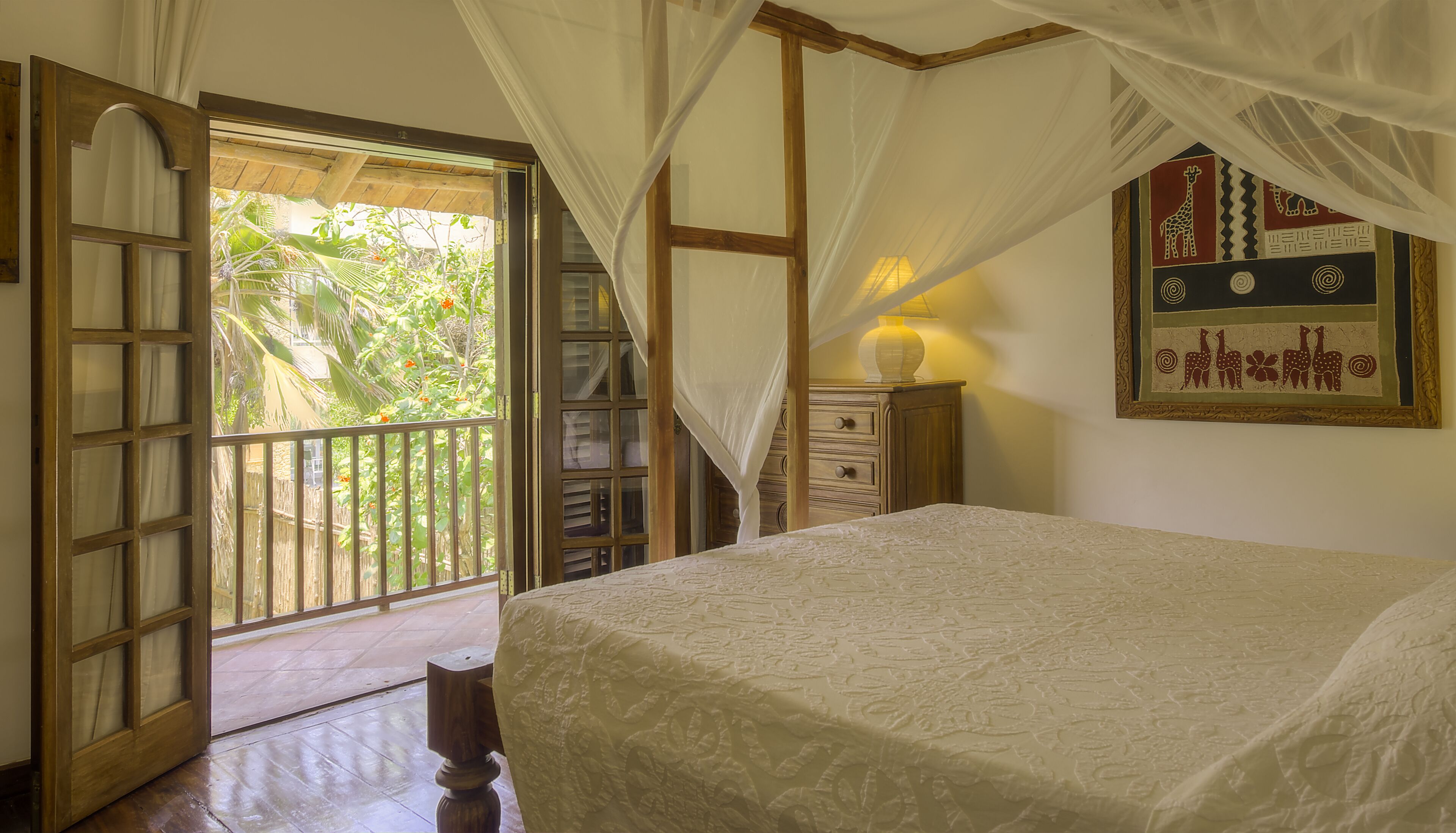 Quarto com cama, mesa de cabeceira, luminária, janela com cortinas e porta para o exterior.