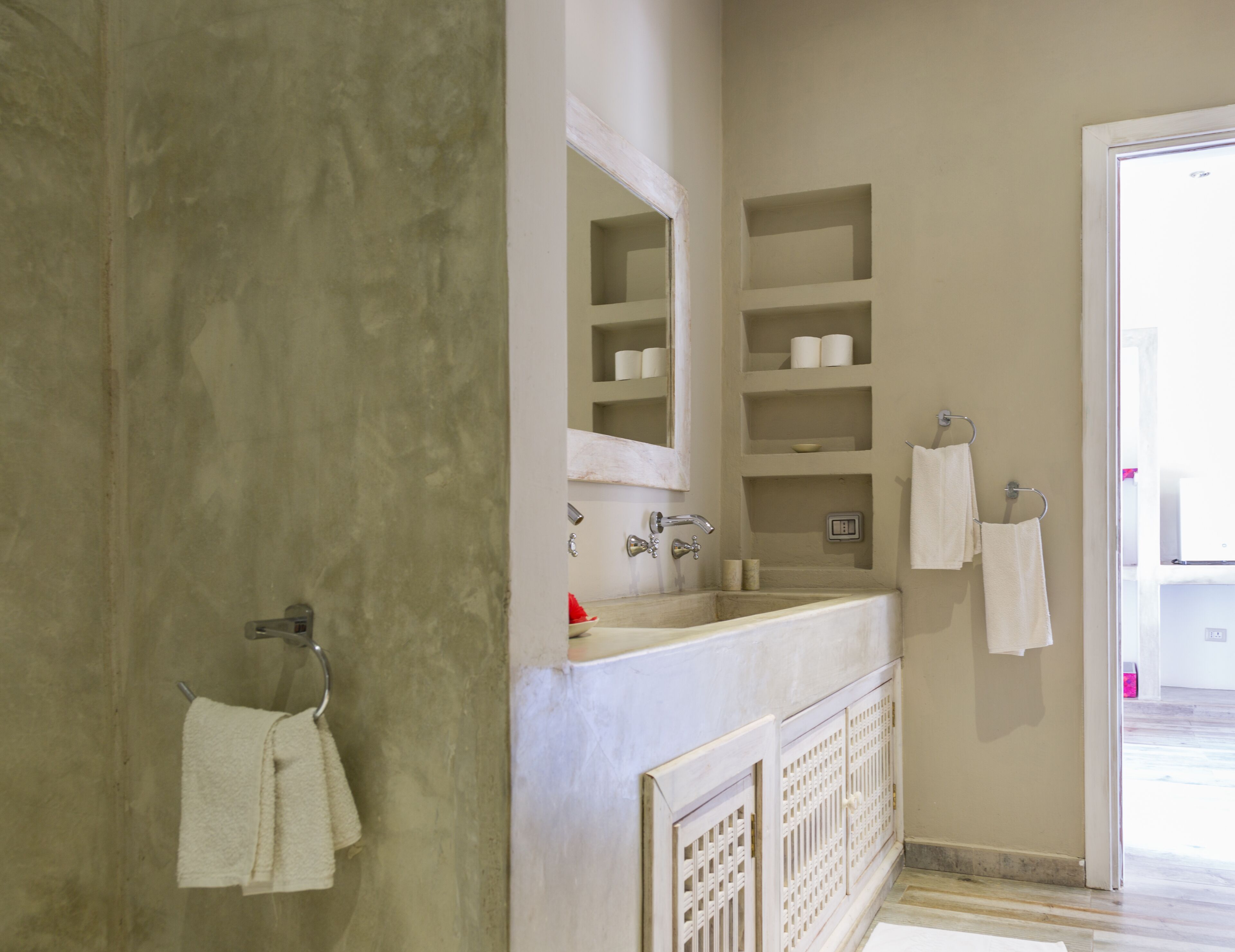 A bathroom with a large mirror, a sink, and shelves with toiletries.